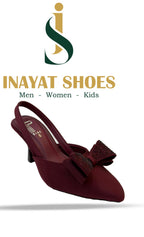 A model wearing black pointed-toe dressy flats with a sparkling pearl strap, styled with formal trousers.