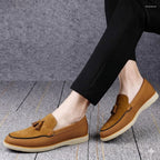 Brown loafers with tassels worn by a person on a gray floor.