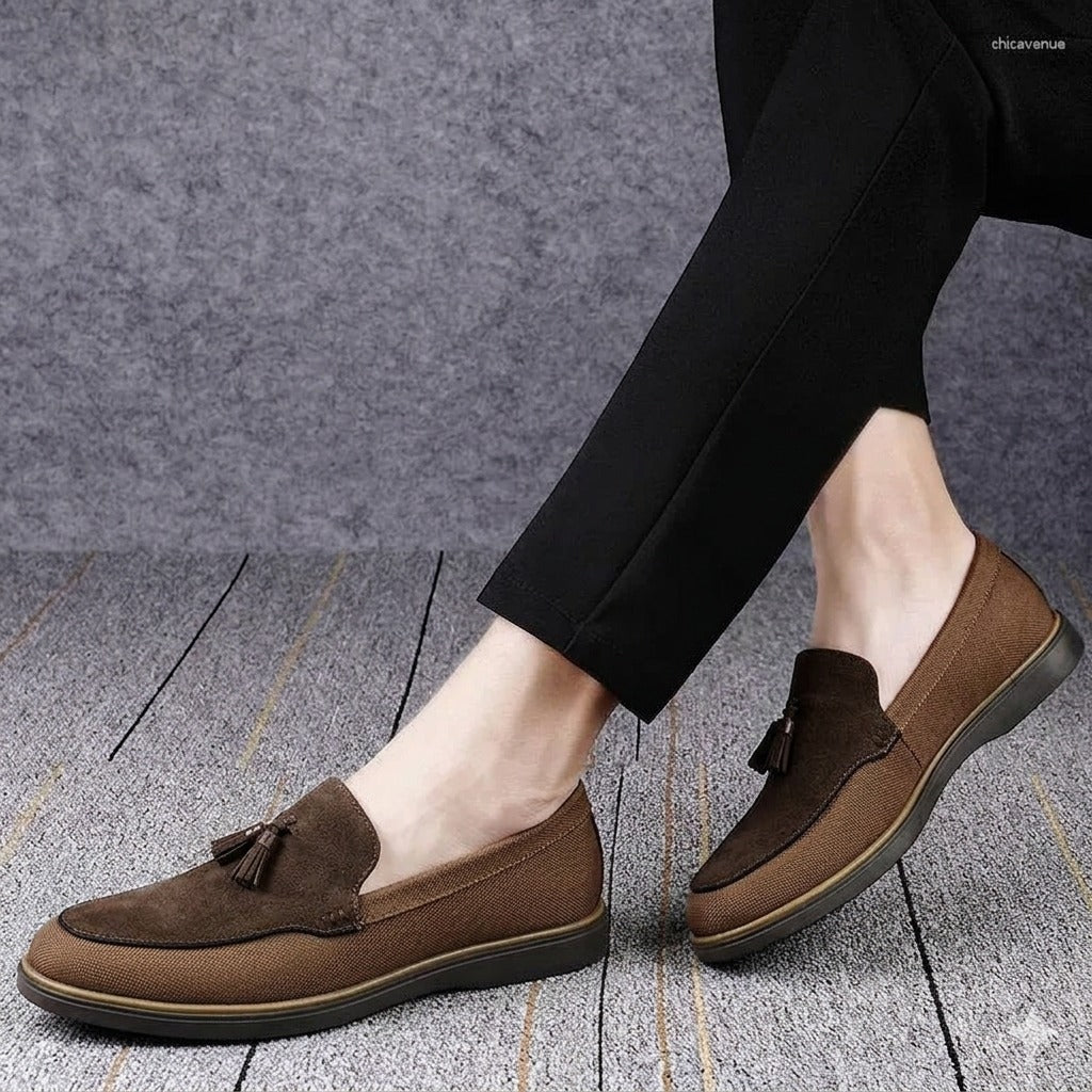Brown loafers worn with black pants on a gray floor.