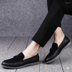 Black loafers worn with black pants on a gray textured floor.