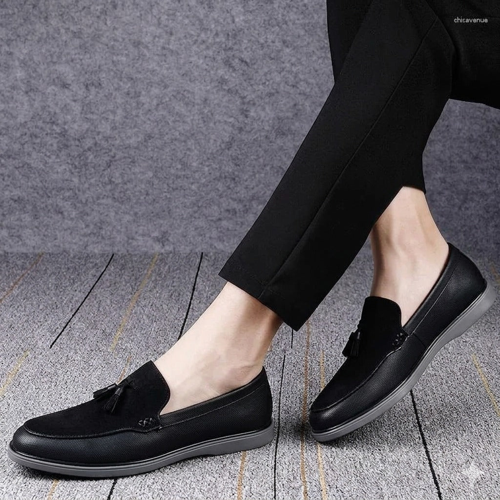 Black loafers worn with black pants on a gray textured floor.