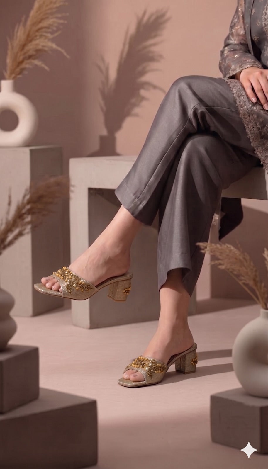 Person wearing gold sandals with floral designs on a neutral background