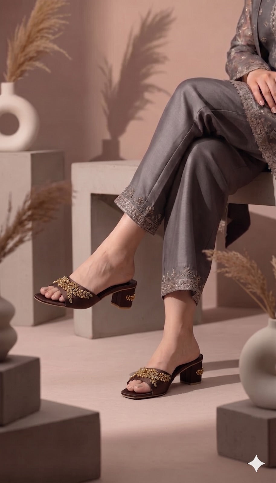 Person wearing decorative sandals in a minimalistic setting with plants and geometric shapes.
