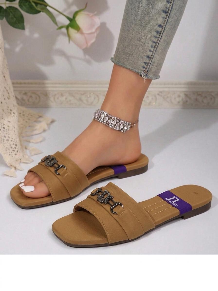 Brown sandals with chain details worn by a person, on a light background.