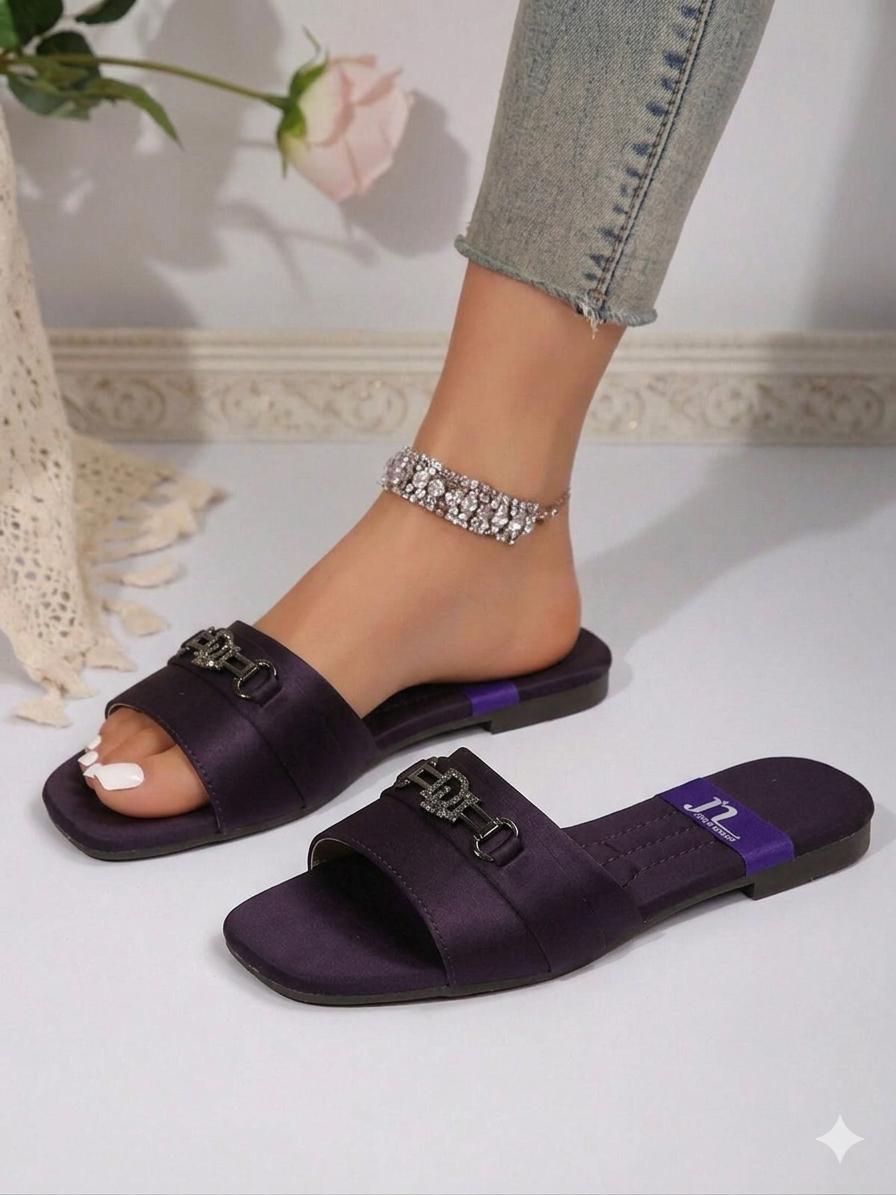 Purple slides with chain details worn by a person, with a blurred background.