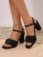 Black high-heeled sandals worn by a person on a neutral background