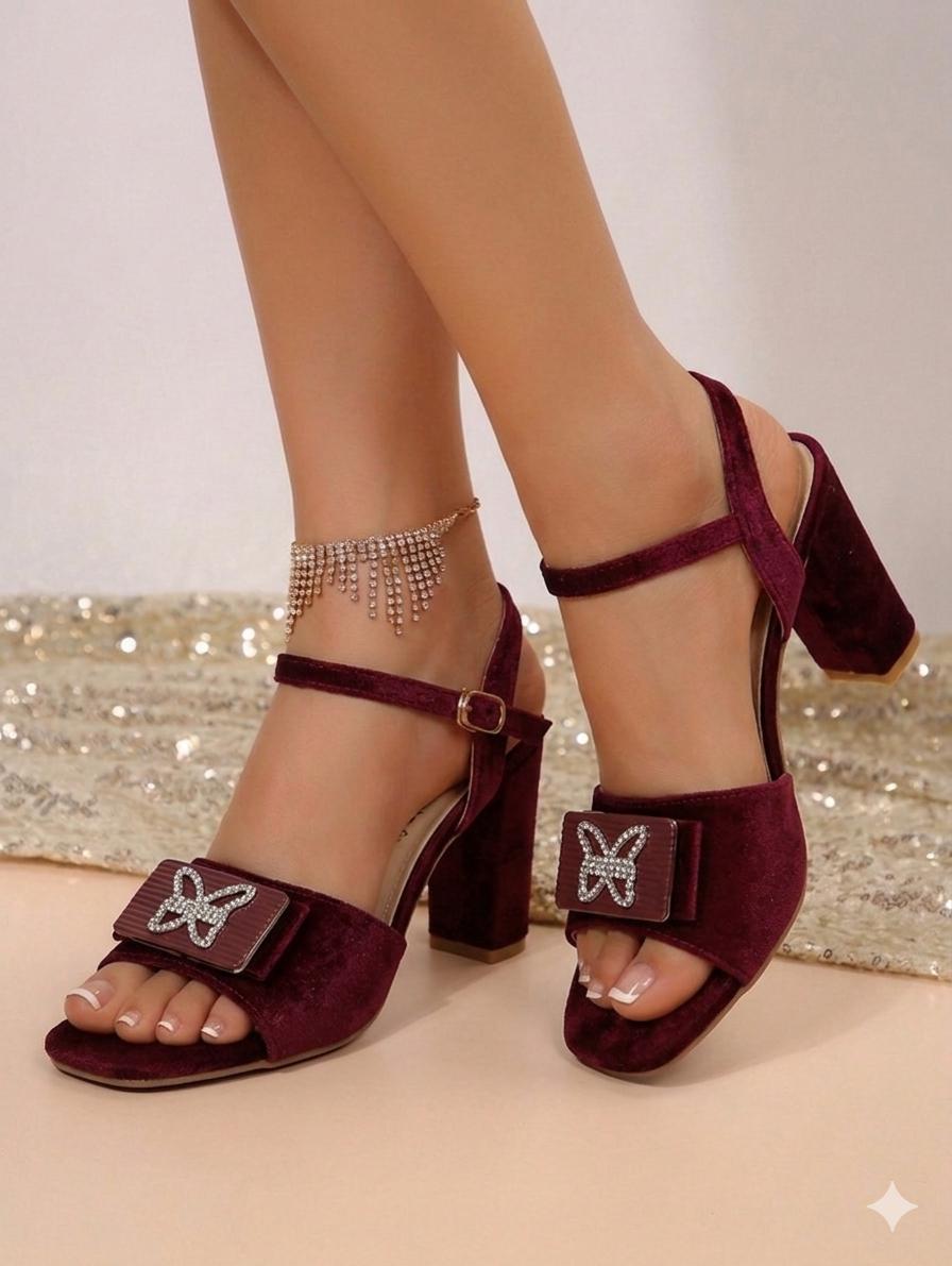 Maroon high-heeled sandals with butterfly details worn by a person on a neutral background
