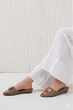 Brown sandals worn with white pants against a light wooden panel background