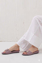 Person wearing light purple sandals with white pants against a light wooden panel background