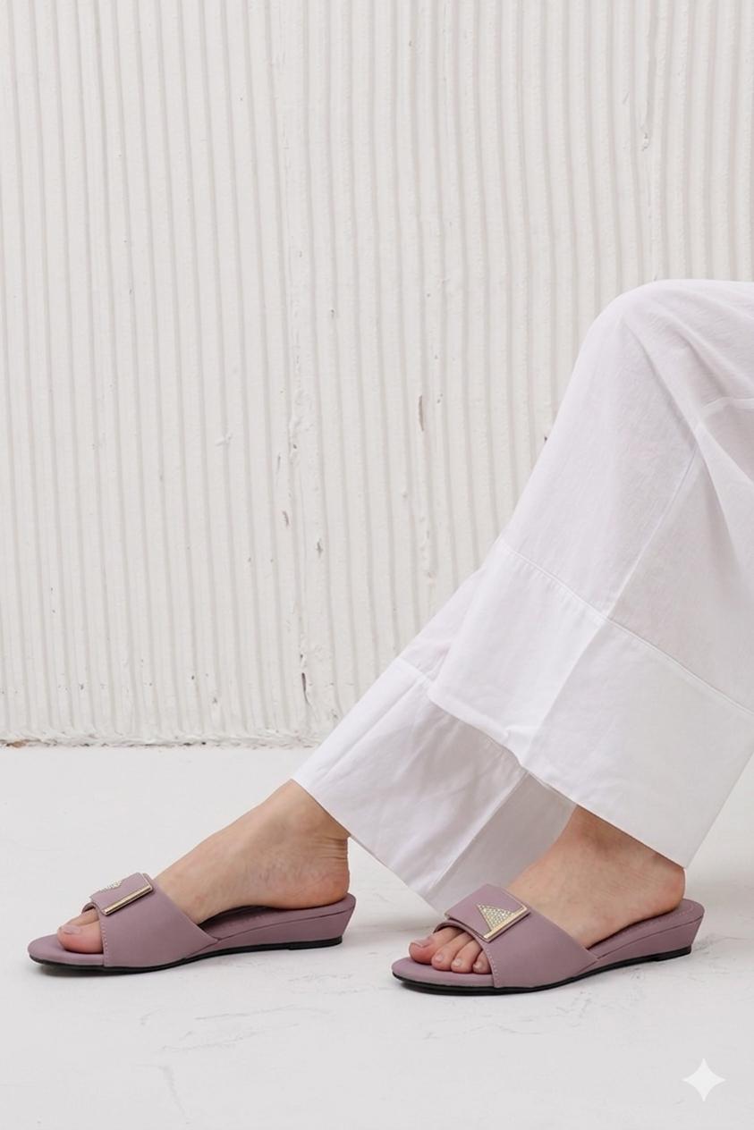Person wearing light purple sandals with white pants against a light wooden panel background