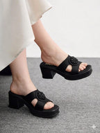 Black sandals with decorative elements worn by a person on a gray floor.
