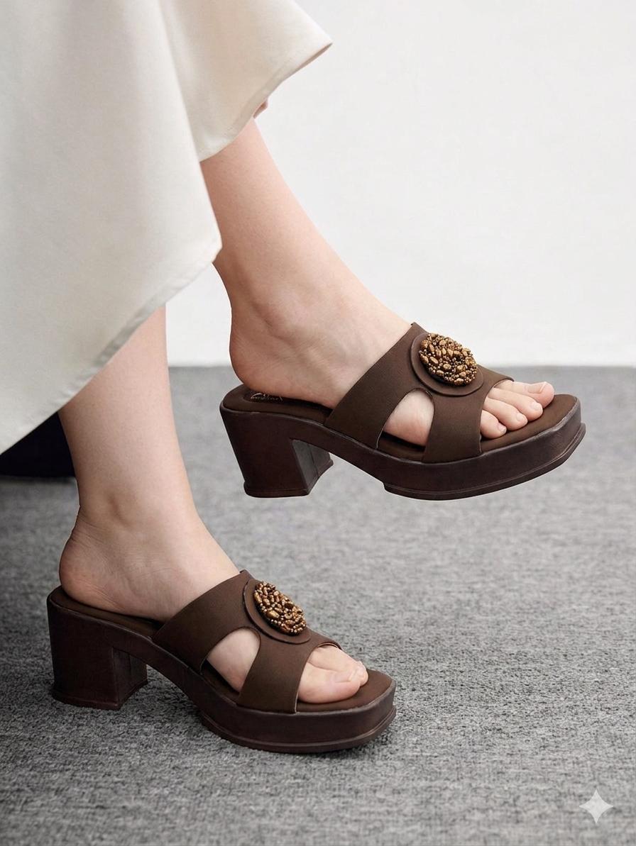 Brown sandals with floral embellishments worn by a person on a gray floor.