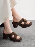 Brown sandals with floral embellishments worn by a person on a gray floor.
