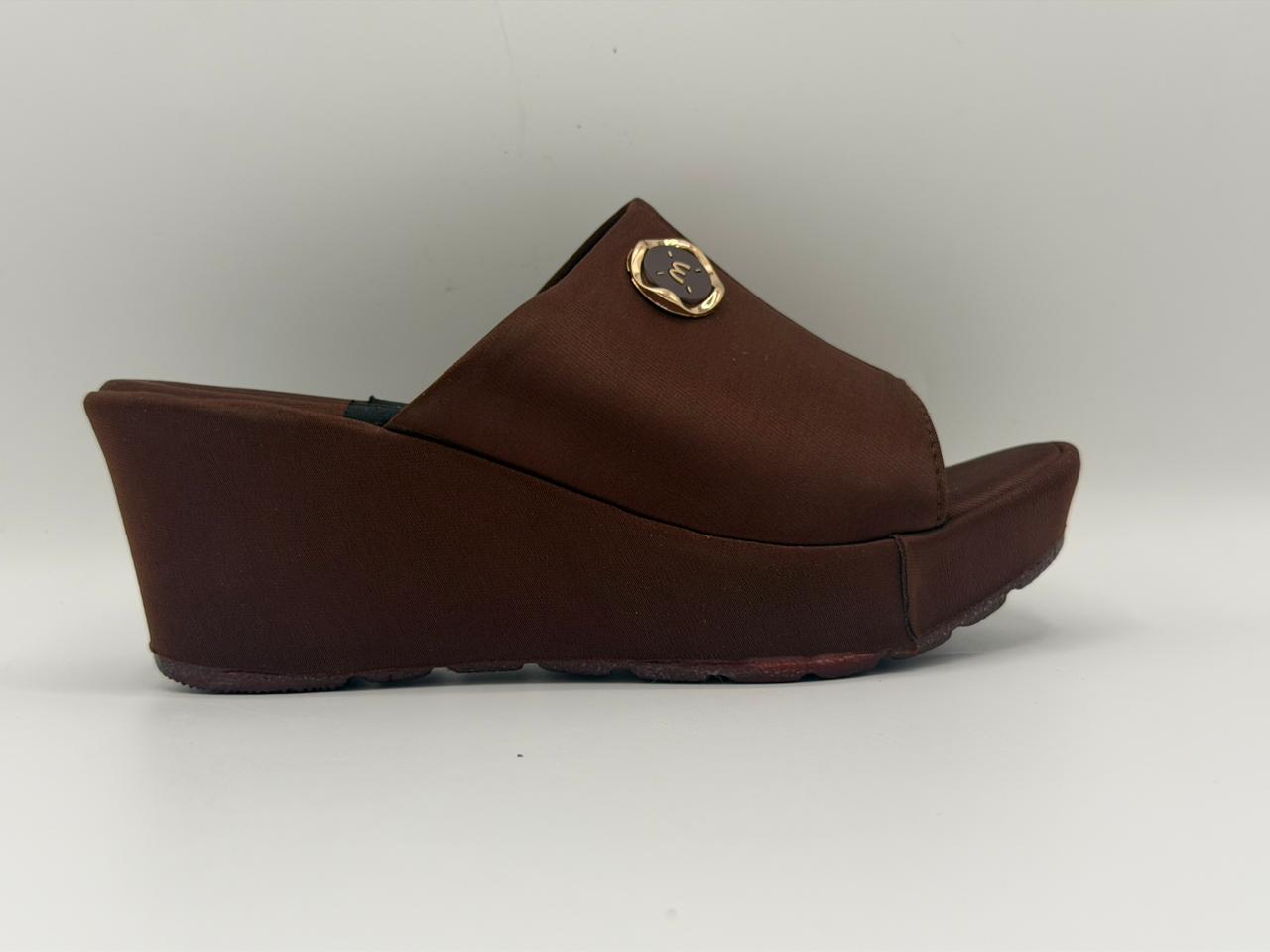 Brown wedge sandal with a gold emblem on a white background