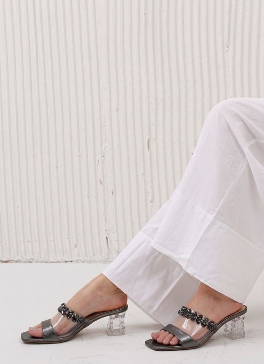 Person wearing transparent high-heeled sandals with clear crystals on a white background