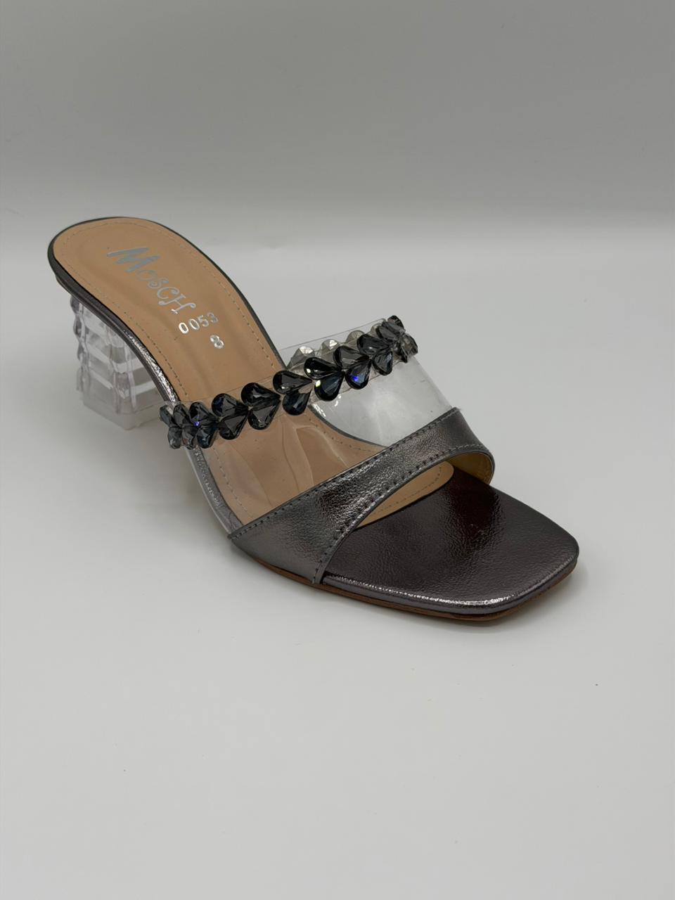 Metallic sandal with clear heel and black embellishments on a light gray background