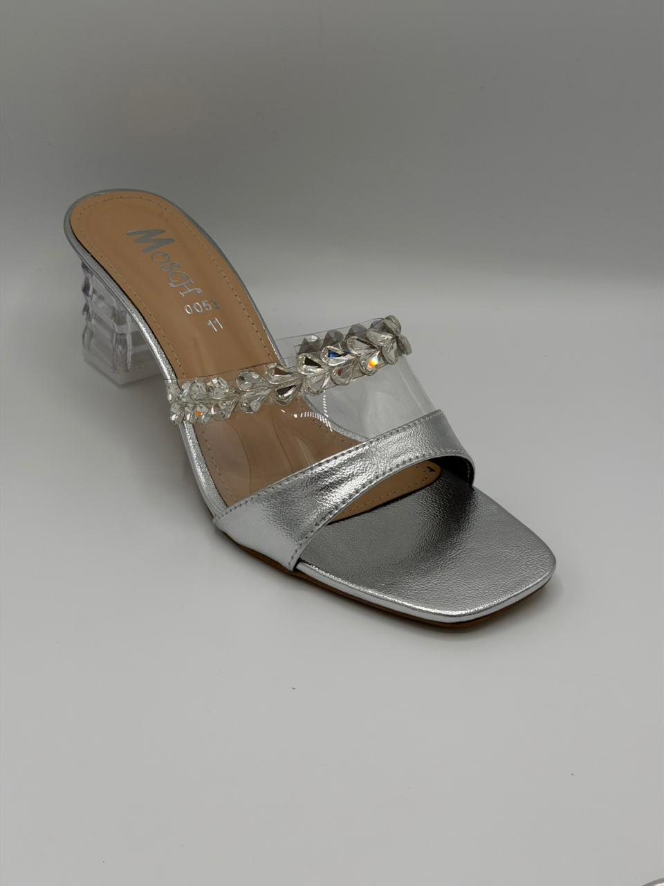 Silver sandal with clear heel and embellishments on a gray background