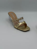 Gold sandal with clear strap and rhinestone embellishments on a light gray background