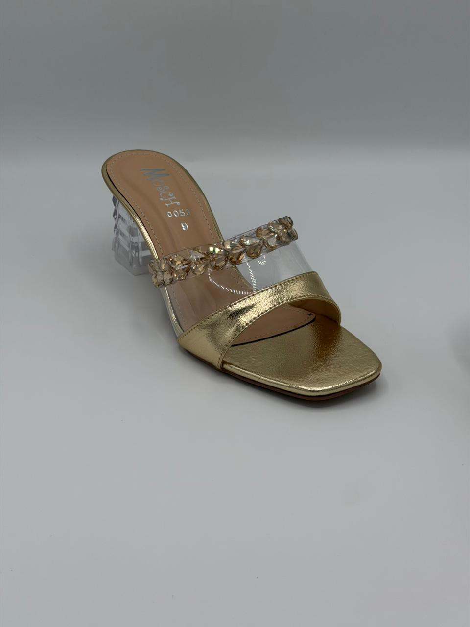 Gold sandal with clear strap and rhinestone embellishments on a light gray background
