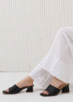 Black open-toe shoes worn with white pants against a light background