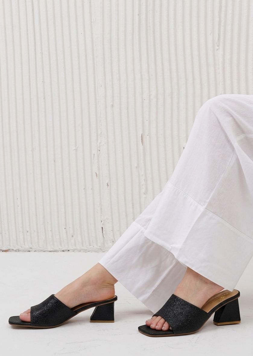 Black open-toe shoes worn with white pants against a light background