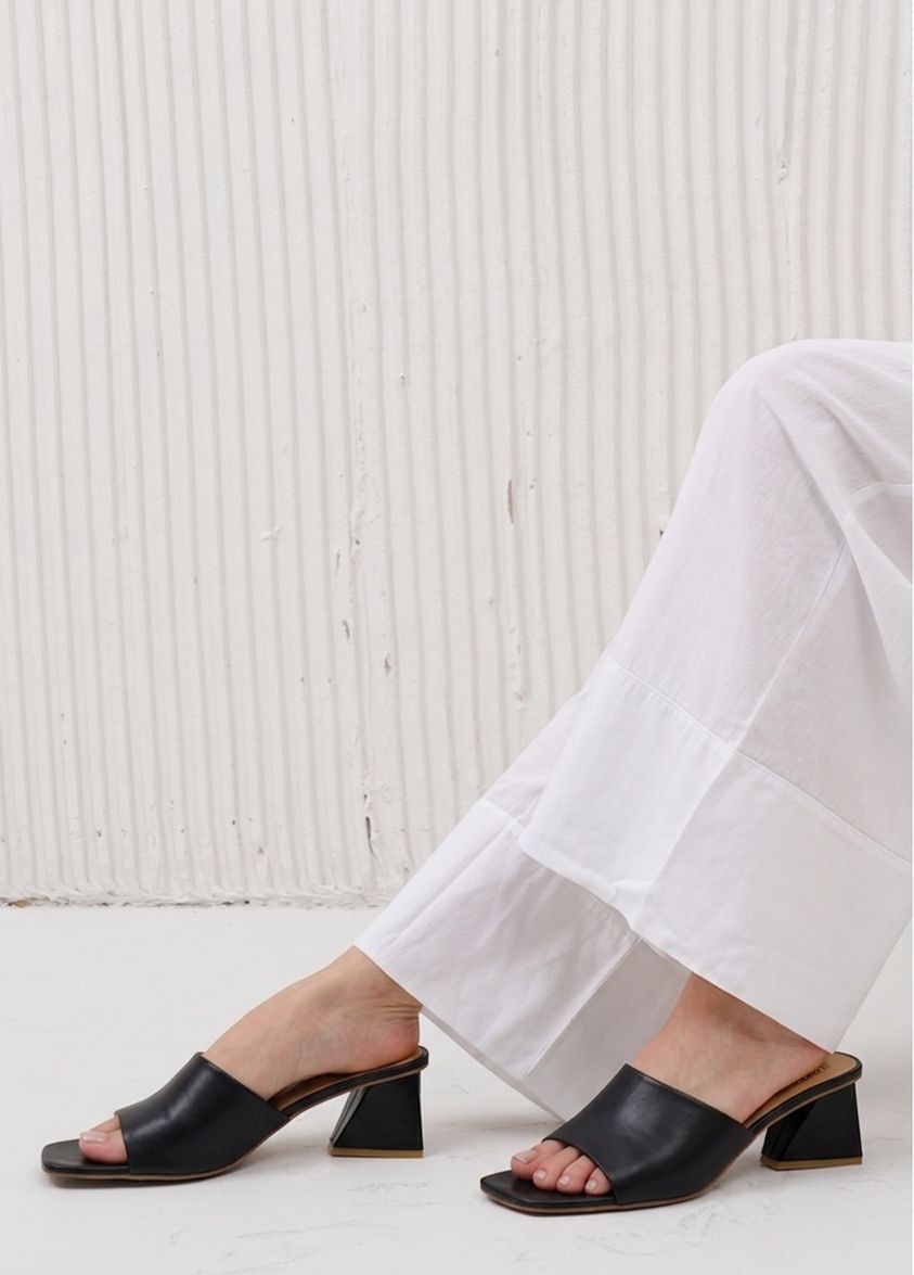 Black open-toe sandals worn with white pants against a light background