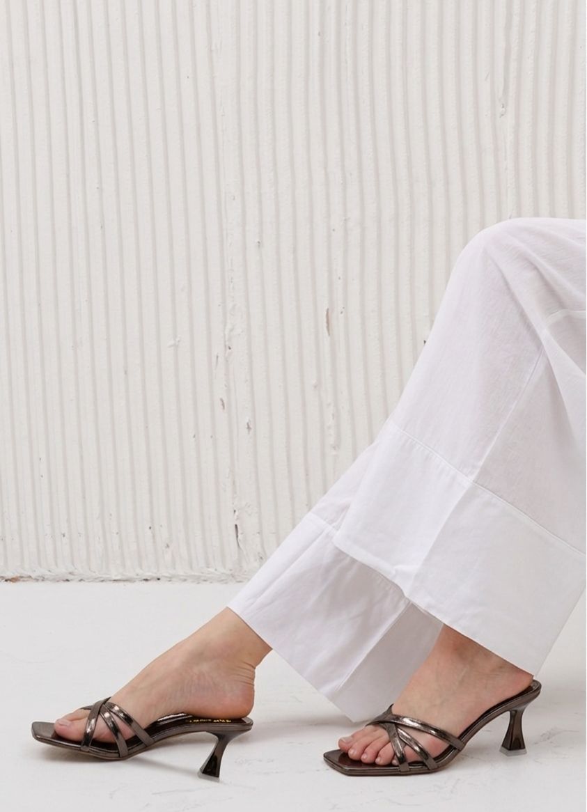 Person wearing black high-heeled sandals with white pants against a light background