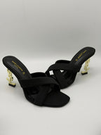 Black high-heeled sandals with gold accents on a light gray background