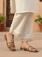 Person wearing white pants with gold embroidery and brown sandals indoors.