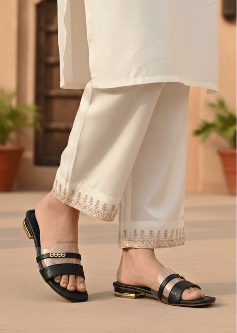 Person wearing white pants with embroidery and black sandals on a neutral background
