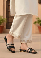 Person wearing white pants with embroidery and black sandals on a neutral background