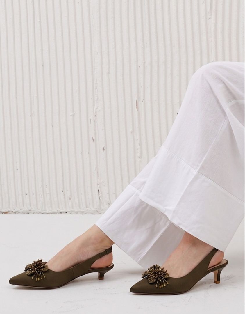 Brown slingback shoes with decorative elements worn with white pants on a light background