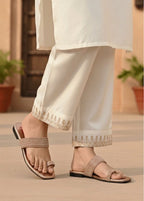 Person wearing white pants with gold embroidery and sandals on a neutral background