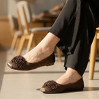 Brown flat shoes with floral decorations worn indoors.