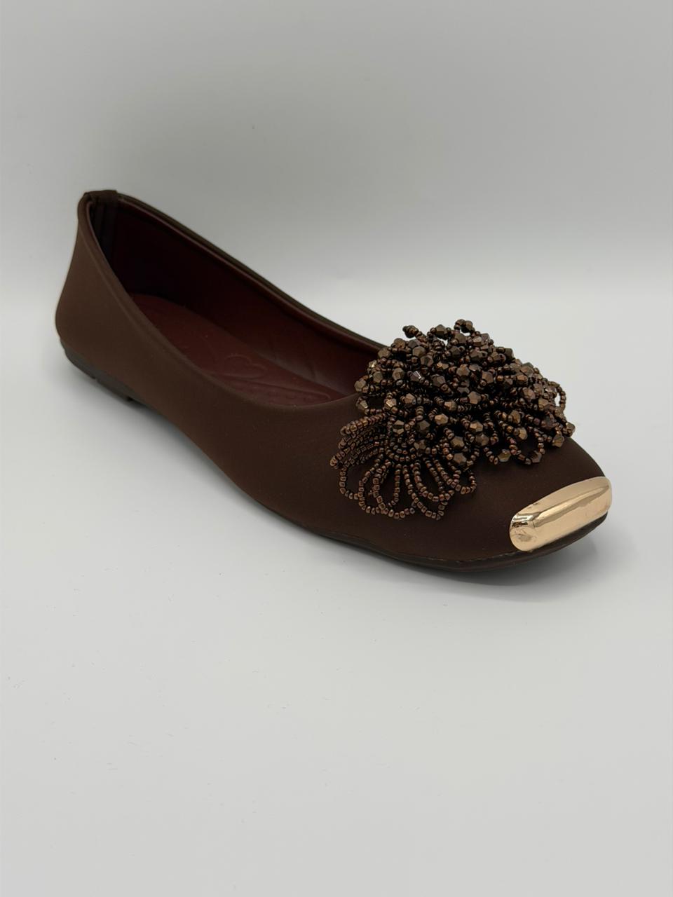 Brown flat shoe with decorative embellishment on a light gray background