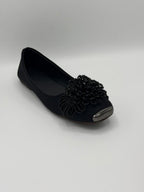 Black flat shoe with decorative flower on a gray background