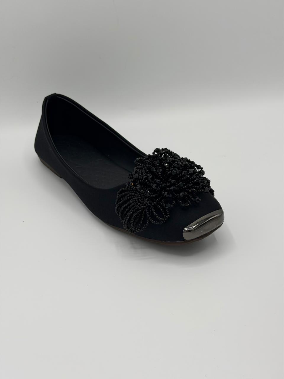 Black flat shoe with decorative flower on a gray background