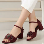 Maroon high-heeled sandals with floral embellishments worn by a person.