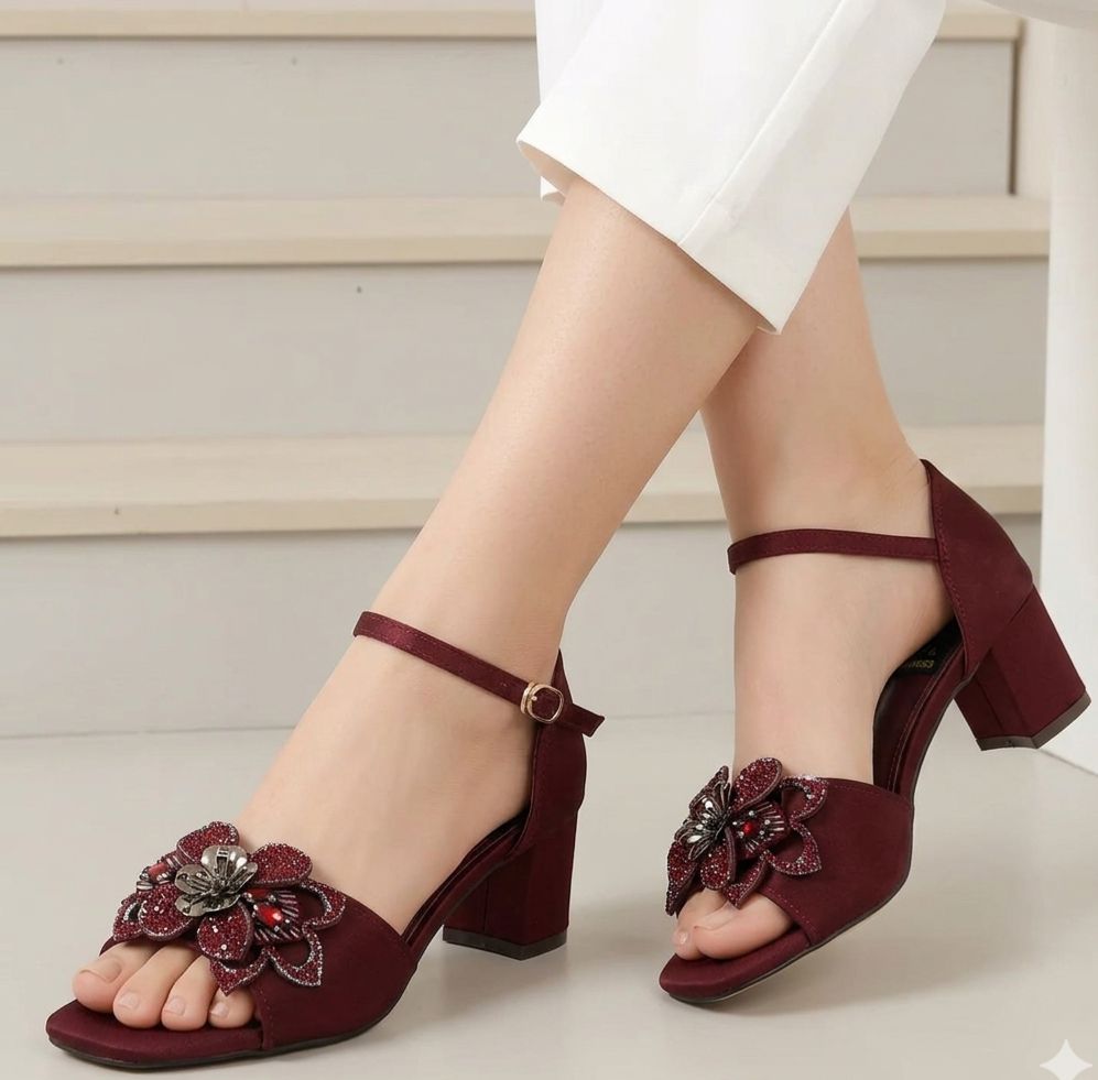 Maroon high-heeled sandals with floral embellishments worn by a person.