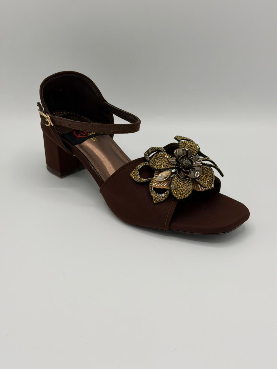 Brown sandal with gold floral embellishments on a light gray background