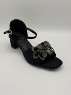 Black sandal with floral embellishment on a light gray background