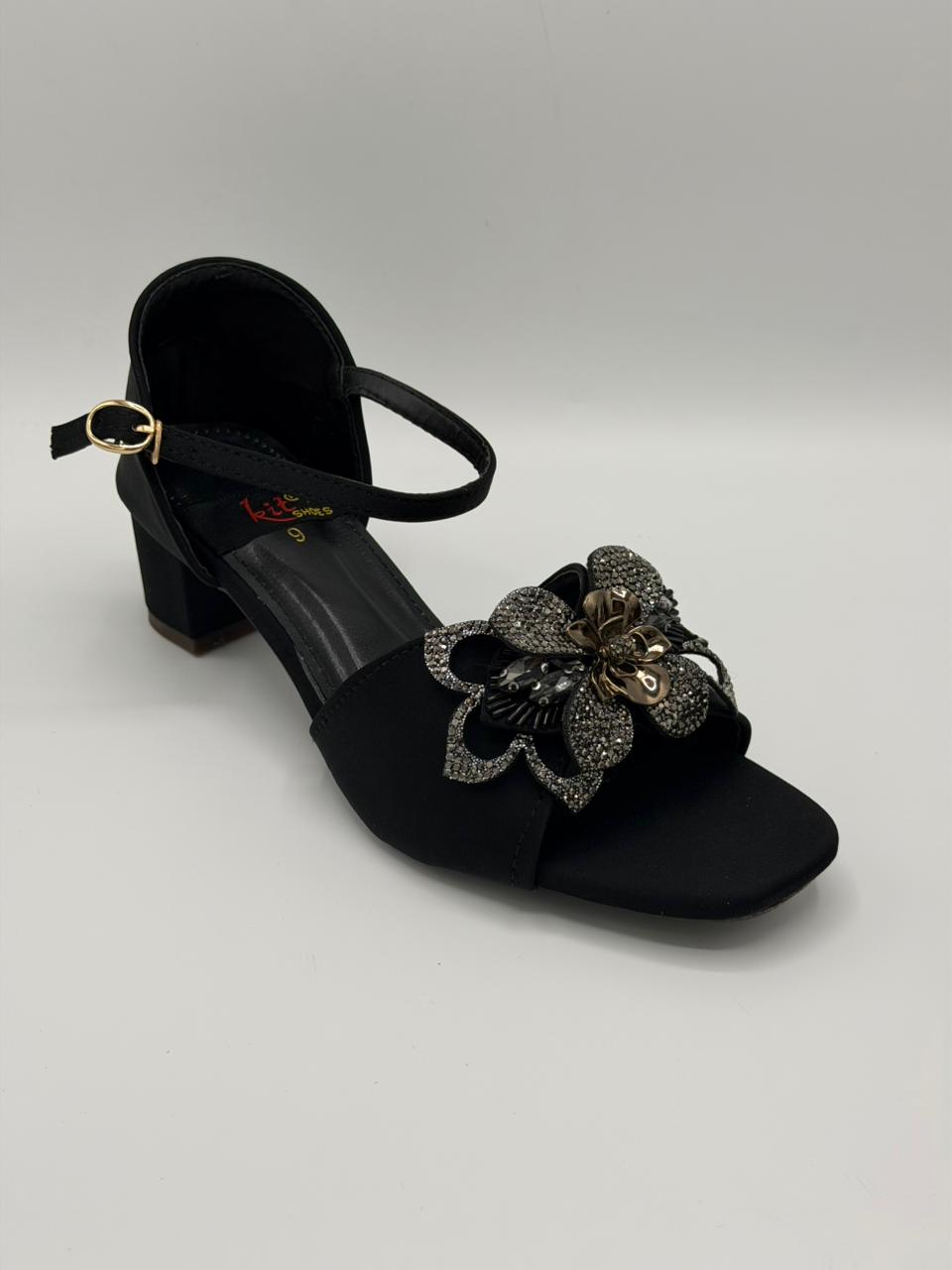 Black sandal with floral embellishment on a light gray background