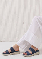 Navy sandals worn with white pants against a light background