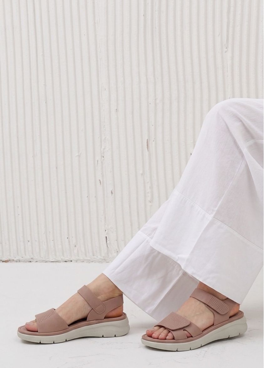 Person wearing pink sandals with white pants against a textured white wall.