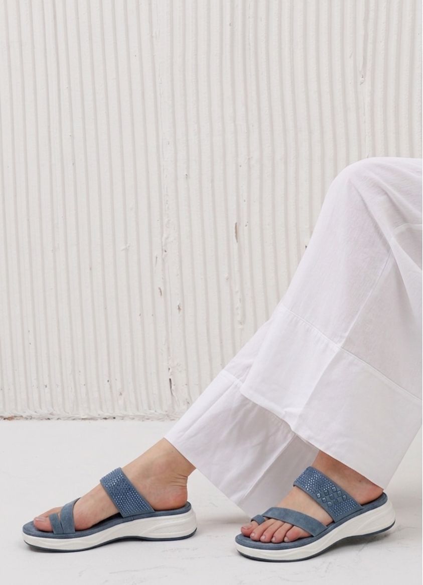 Person wearing blue sandals with white soles on a light wooden floor.