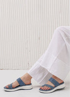 Person wearing blue sandals with white soles on a light wooden floor.