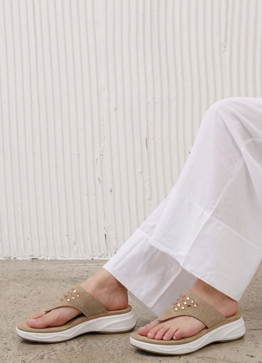 Person wearing beige sandals with white soles on a light wooden floor.