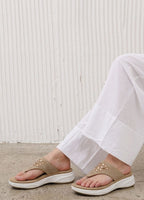 Person wearing beige sandals with white soles on a light wooden floor.