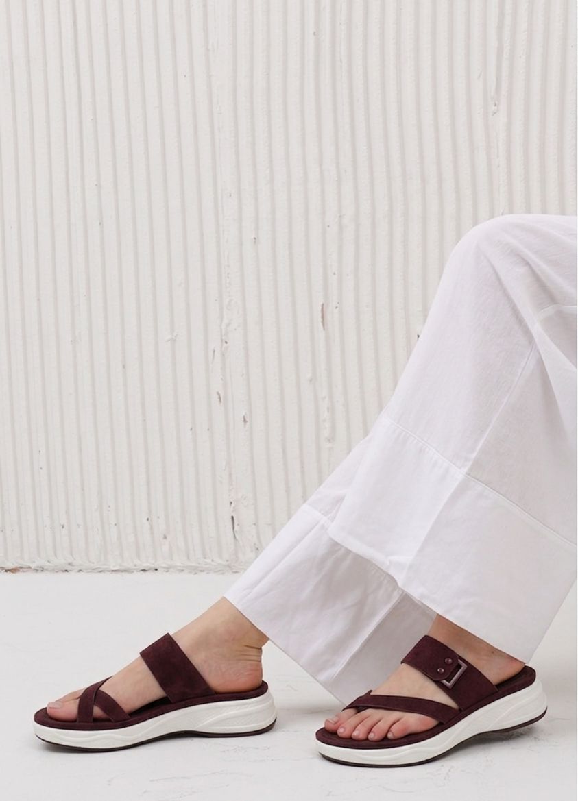 Person wearing brown sandals with white soles on a light background