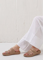 Beige sandals with gold buckles worn with white pants against a light background